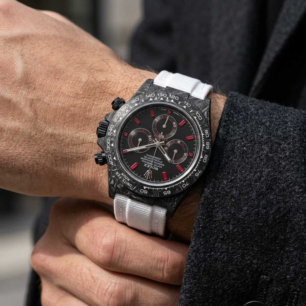 Black forged carbon chronograph with red baguette stone markers and a white strap on the wrist as a shirt cuff is fastened
