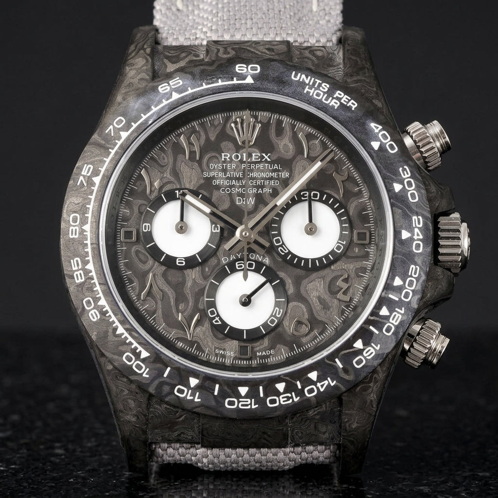 Black forged-carbon chronograph with a grey carbon dial on its grey canvas strap, worn on the wrist below a dark suit cuff