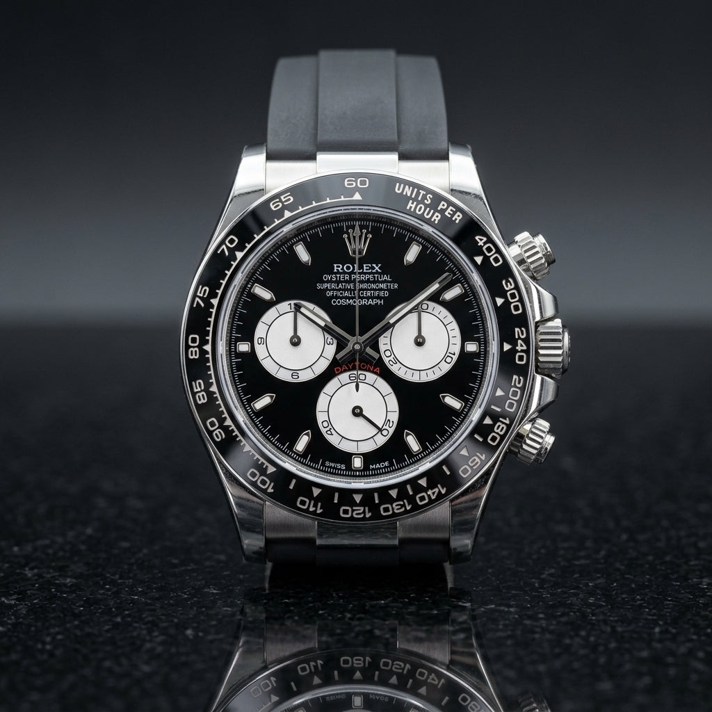 Steel chronograph with a black dial and white counters on its black rubber strap, worn on the wrist below a dark suit cuff