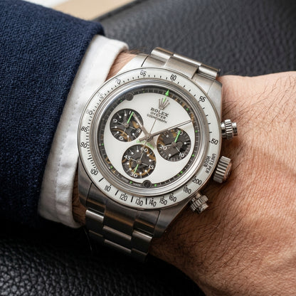 Steel chronograph with a white dial and green accents on the wrist below a dark suit cuff