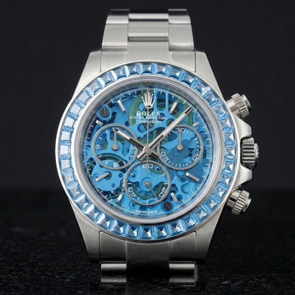Steel skeleton chronograph with a blue stone bezel on its steel bracelet, worn on the wrist below a dark suit cuff