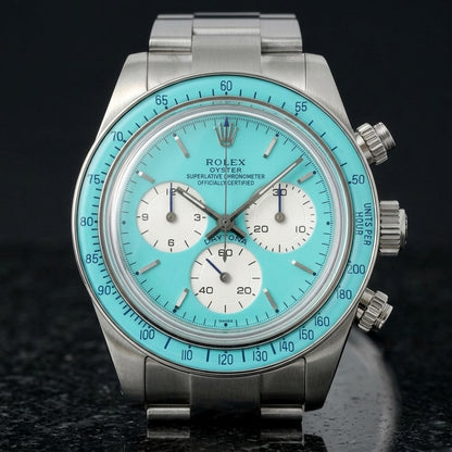 Steel chronograph with a turquoise dial and bezel on the wrist below a dark suit cuff