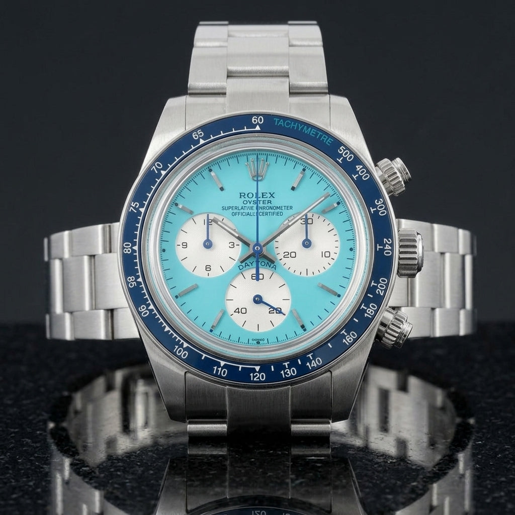 Steel chronograph with a turquoise dial and a navy blue bezel, upright on polished white marble