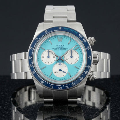 Steel chronograph with a turquoise dial and a navy blue bezel, upright on polished white marble