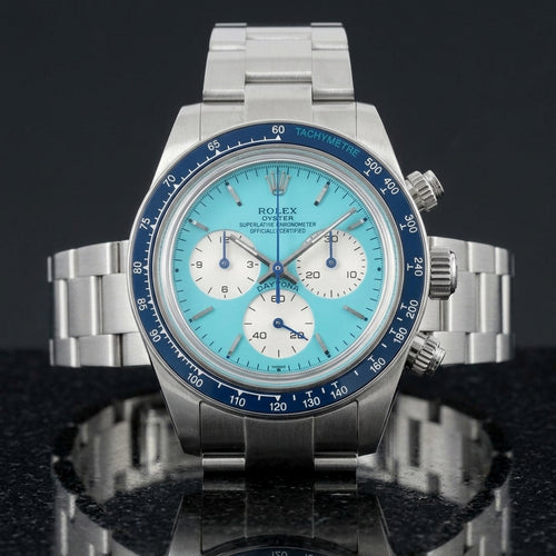 Steel chronograph with a turquoise dial and a navy blue bezel, upright on polished white marble