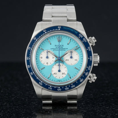 Steel chronograph with a turquoise dial on its steel bracelet, worn on the wrist below a dark suit cuff