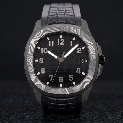 Forged-carbon watch with a black dial on its black rubber strap, worn on the wrist below a dark suit cuff