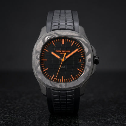 Black forged-carbon grid-dial watch with orange batons and a black rubber strap, upright on polished black granite