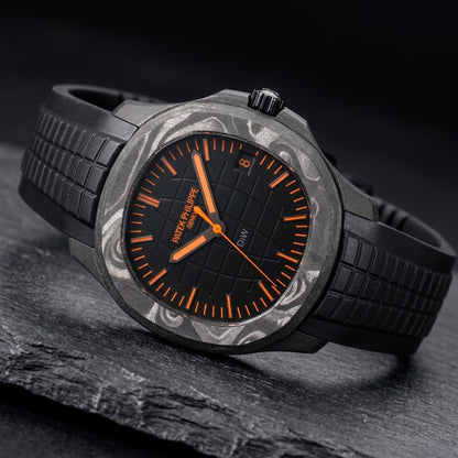 Black forged-carbon grid-dial watch at a three-quarter angle on dark slate, grey marbling across the bezel and a black fluted crown