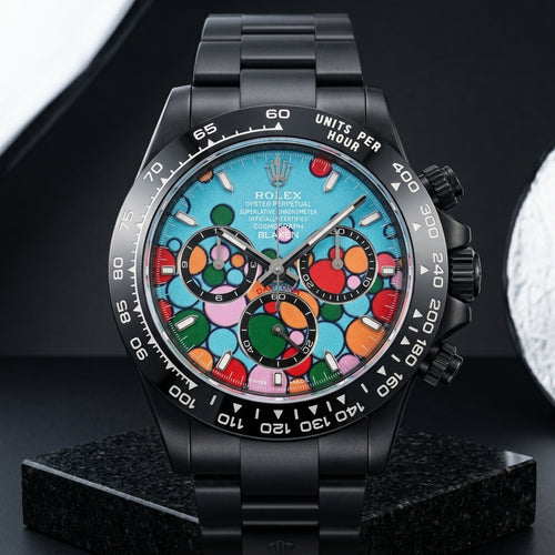 Black DLC chronograph with a turquoise dial of red, orange, green and pink circles, standing upright on polished black granite