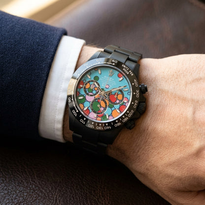 Black DLC chronograph with a turquoise bubble dial on a black steel bracelet, worn on the wrist below a navy suit cuff
