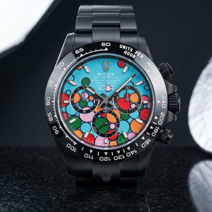 Black DLC chronograph with a turquoise bubble dial on a black steel bracelet, worn on the wrist below a navy suit cuff