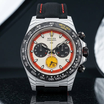 White forged carbon chronograph with a black bezel, a cream dial in a red-orange ring and a yellow 73 counter, upright on polished black granite