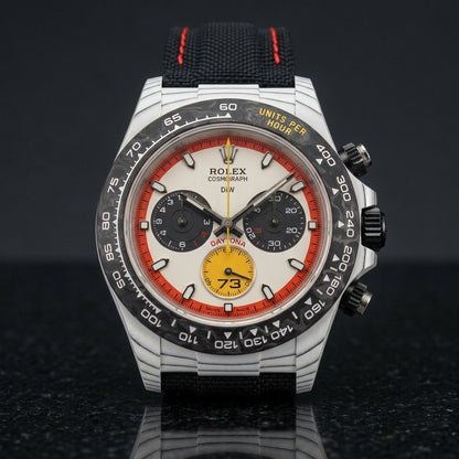 White carbon chronograph on its black canvas strap with red stitching, worn on the wrist below a navy suit cuff
