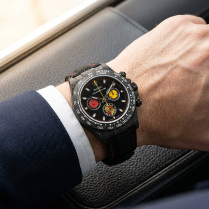 Black forged-carbon chronograph on a red-stitched strap worn under a suit cuff