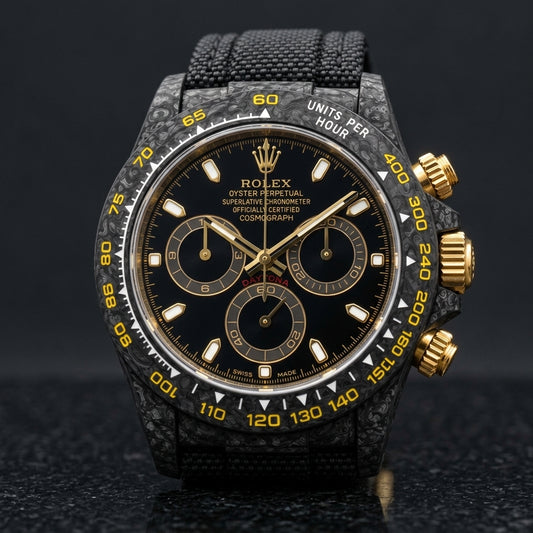 Black forged carbon chronograph with a black dial printed in gold and a yellow tachymeter scale, upright on polished black granite
