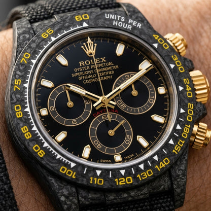 Macro of the black dial with gold-framed markers and three gold-ringed counters, inside the yellow-printed carbon bezel