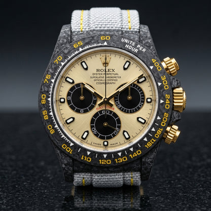 Black forged carbon chronograph with a champagne dial, black counters and a yellow tachymeter scale, upright on polished black granite