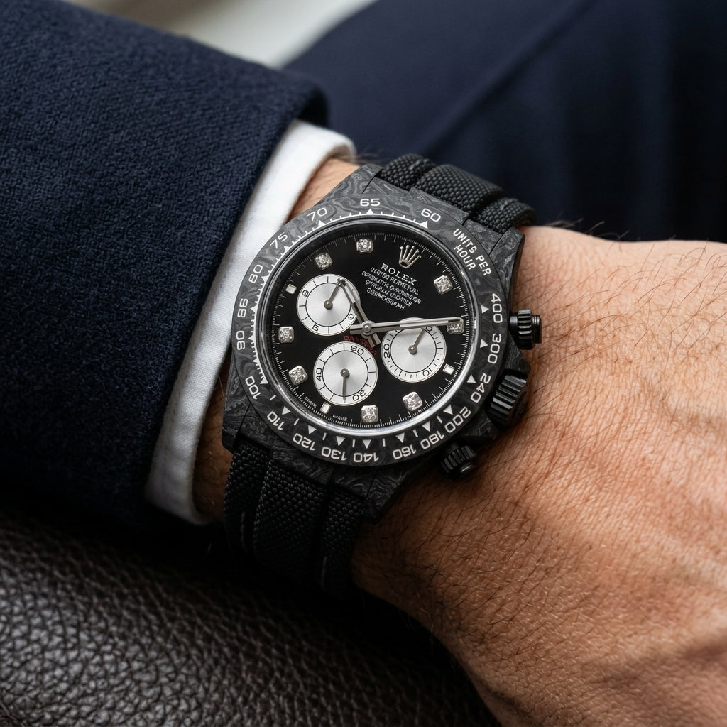 Black carbon chronograph on its black beaded fabric strap with grey stitching, worn on the wrist below a dark suit cuff