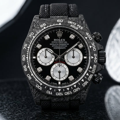 Black carbon chronograph on its black beaded fabric strap with grey stitching, worn on the wrist below a dark suit cuff
