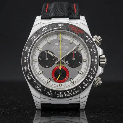 White carbon chronograph on its black canvas strap with red stitching, worn on the wrist below a navy suit cuff