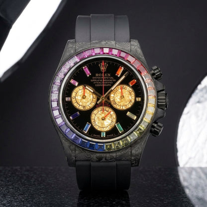 Rainbow bezel carbon chronograph on a black rubber strap worn under a suit cuff