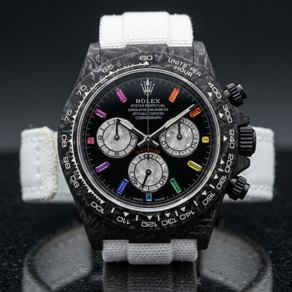Black forged carbon chronograph with a carbon tachymeter bezel and a black dial with rainbow stone markers, upright on polished black granite