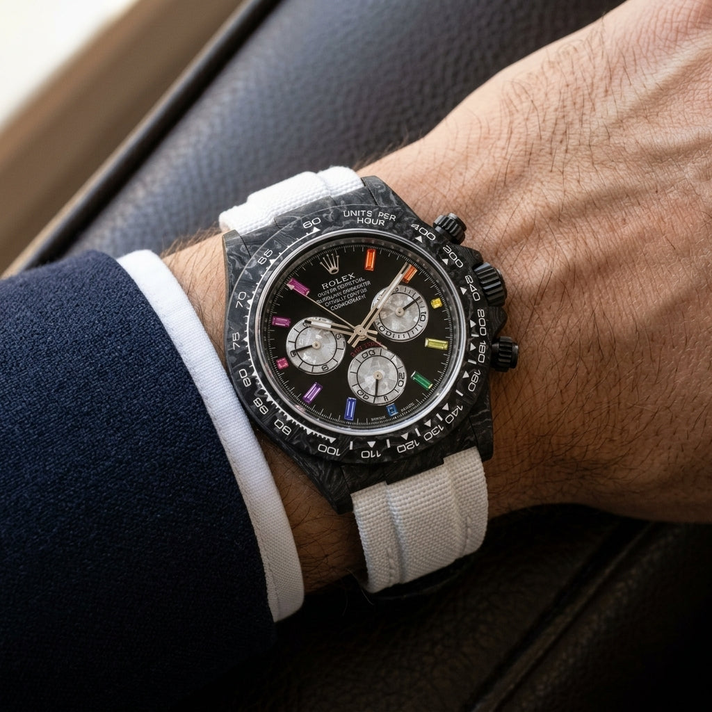 Black carbon chronograph with rainbow stone markers on its white woven strap, worn on the wrist below a dark suit cuff
