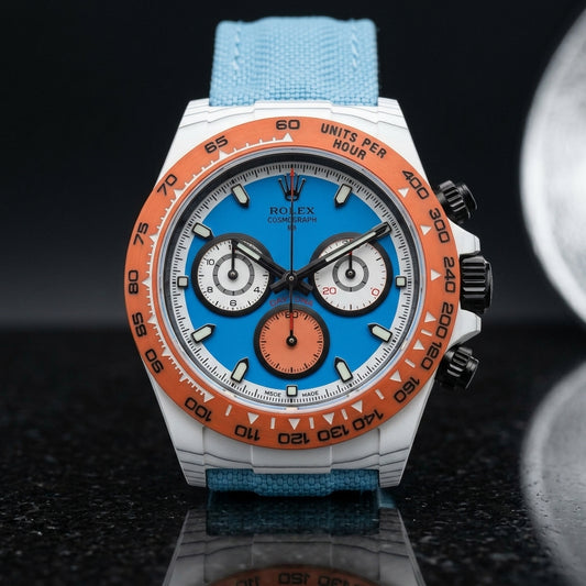 White forged carbon chronograph with an orange bezel, a sky-blue dial and an orange counter at six, upright on polished black granite