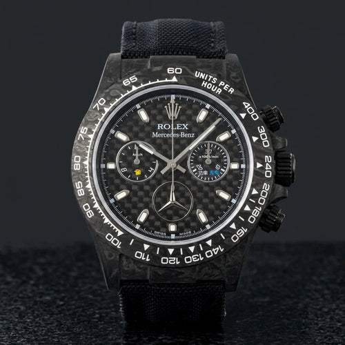 Black forged carbon chronograph with a woven carbon-fibre dial and a three-pointed star emblem, upright on polished black granite