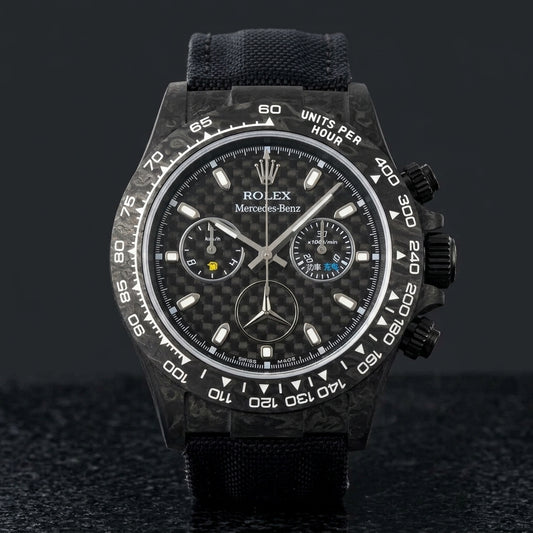 Black forged carbon chronograph with a woven carbon-fibre dial and a three-pointed star emblem, upright on polished black granite