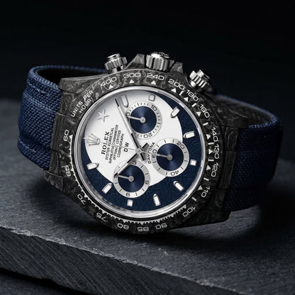 Forged-carbon chronograph at a three-quarter angle, navy sun-brushed counters and navy strap visible