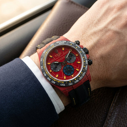 Red forged-carbon chronograph on a black woven strap with yellow stitching, worn under a cuff