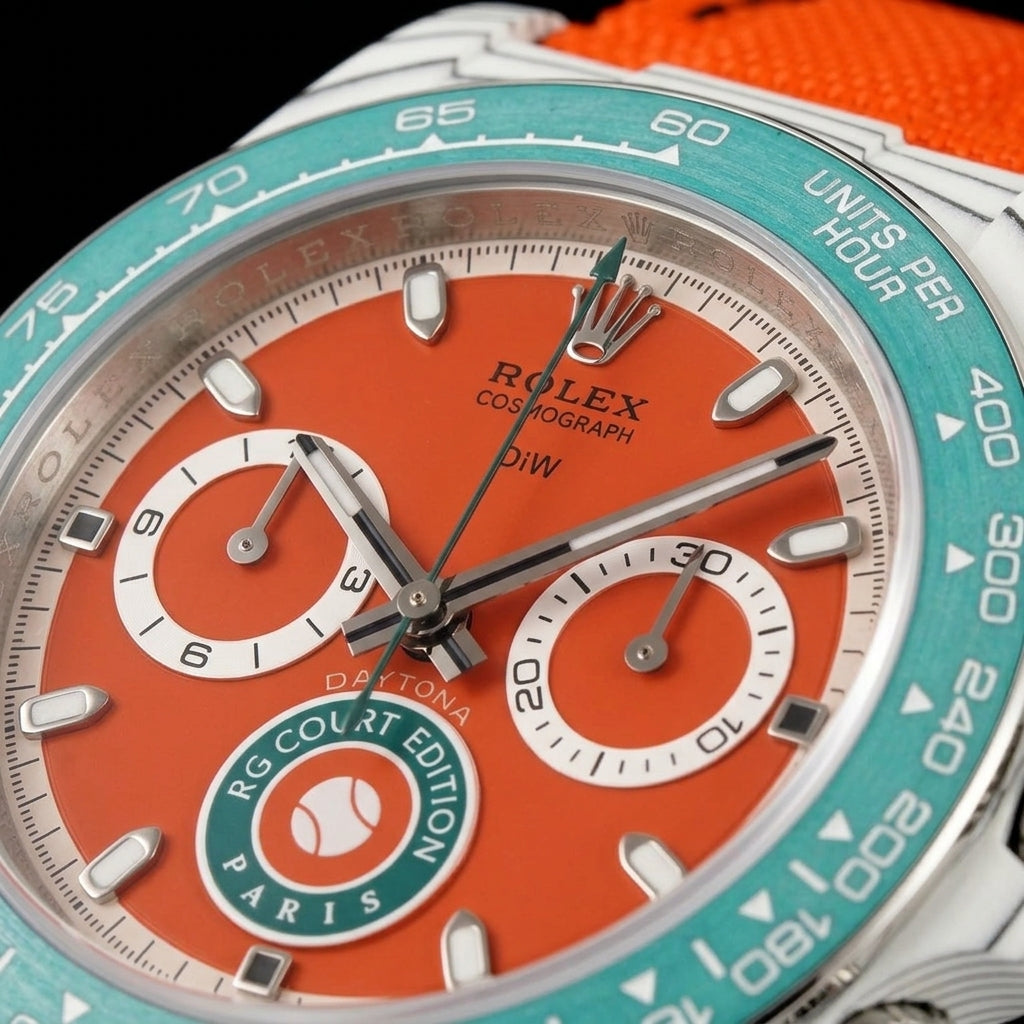 Macro of the clay-red dial with the green tennis badge at six and two white-ringed counters inside the teal bezel