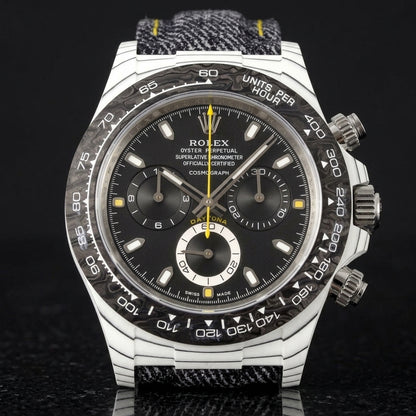 White carbon chronograph with a black dial on its denim strap with yellow stitching, worn on the wrist below a dark suit cuff