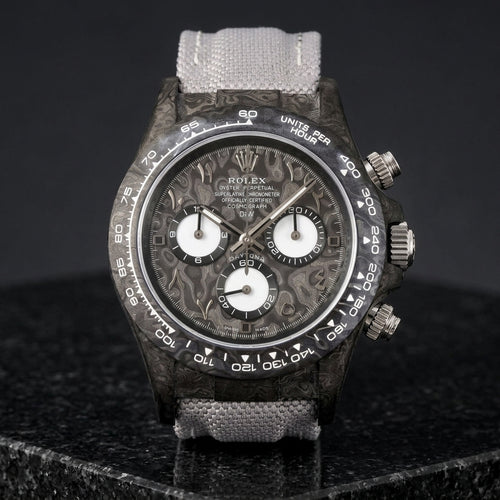 Black forged-carbon chronograph with a grey carbon dial, steel Eastern Arabic numerals and white counters, upright on polished black granite