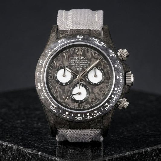 Black forged-carbon chronograph with a grey carbon dial, steel Eastern Arabic numerals and white counters, upright on polished black granite