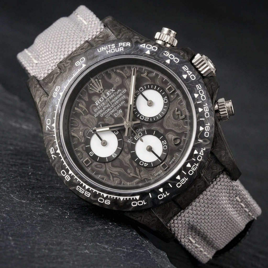 Black forged-carbon chronograph at a three-quarter angle on dark slate, grey veining on its flank beside the polished steel crown and pushers