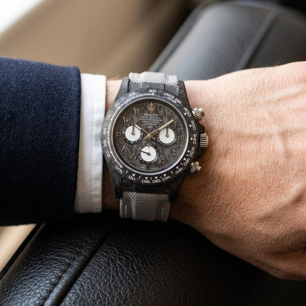 Black forged-carbon chronograph with a grey carbon dial on its grey canvas strap, worn on the wrist below a dark suit cuff