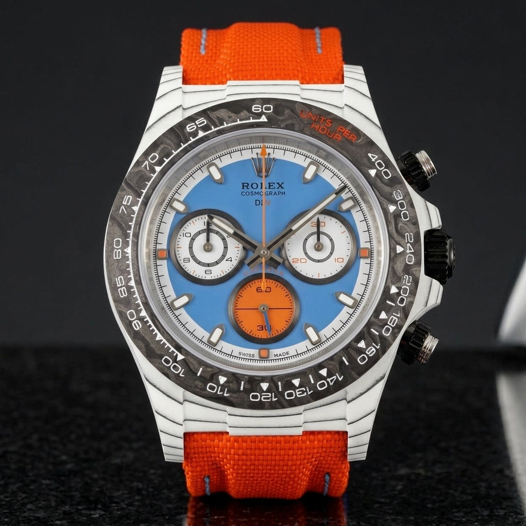 White carbon chronograph with a sky-blue dial, an orange counter and a black forged-carbon bezel, upright on polished black granite
