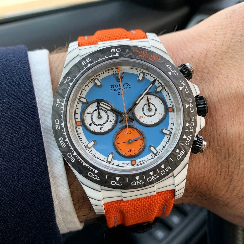 White carbon chronograph with a sky-blue dial on its orange canvas strap, worn on the wrist below a dark suit cuff