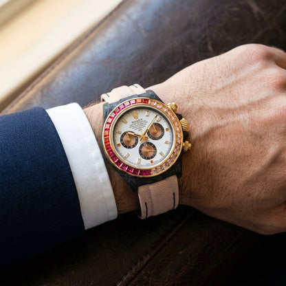 White dial carbon chronograph on a blush fabric strap worn under a suit cuff