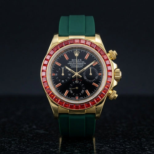 Gold chronograph with a red stone bezel and a black dial on a dark green rubber strap, upright on polished black granite