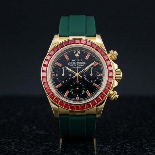 Gold chronograph with a red stone bezel and a black dial on a dark green rubber strap, upright on polished black granite
