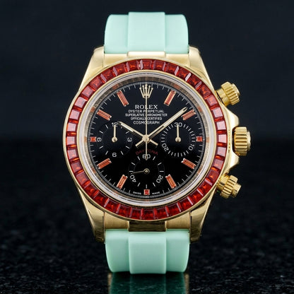 Gold chronograph with a red stone bezel and a black dial on a mint-green rubber strap, upright on polished black granite