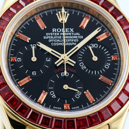 Macro of the black dial with orange stone markers and three black counters inside the ring of red baguette-cut stones