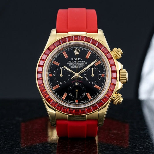 Gold-tone chronograph with a red stone bezel and a black dial on a red rubber strap, upright on polished black granite