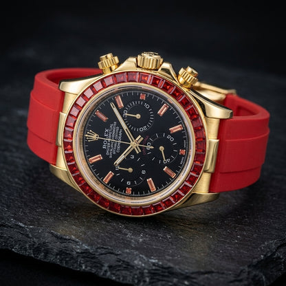 Gold-tone chronograph at a three-quarter angle on dark slate, the fluted crown and pushers beside the ring of red baguette-cut stones