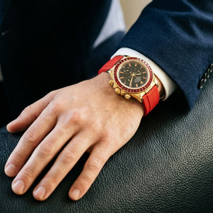 Gold-tone chronograph with a red stone bezel on its red rubber strap, worn on the wrist below a dark suit cuff