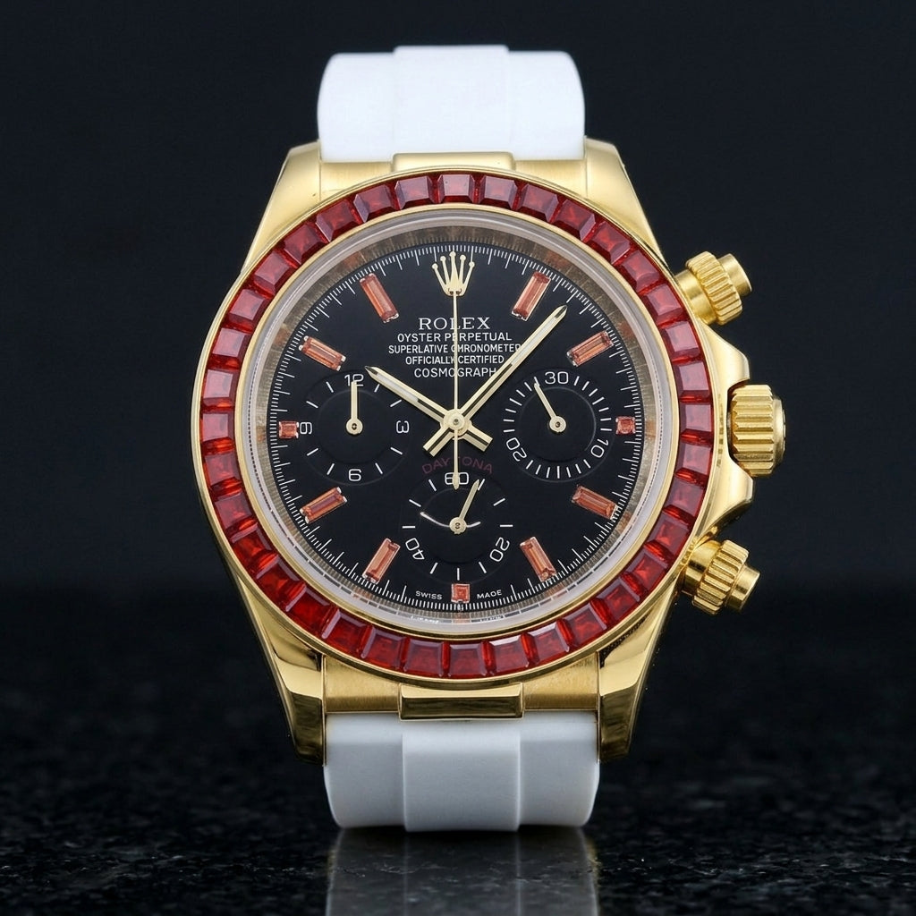 Gold-tone chronograph with a red baguette-stone bezel and a black dial on a white rubber strap, upright on polished black granite